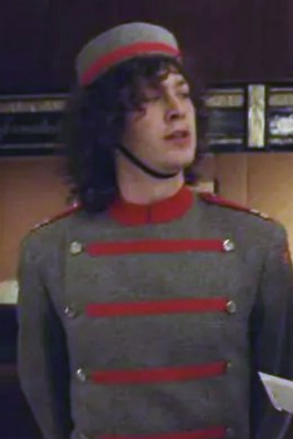 A young Ebon Moss-Bachrach in a bellhop uniform with longer curly hair