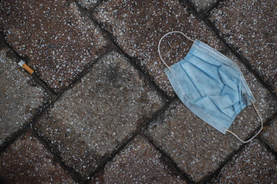 FILE - In this June 18, 2020, file photo a discarded face mask and cigarette butt litter the sidewalk outside the Eastern Market in Washington. On Friday, June 26, Vice President Mike Pence said Americans should look to their state and local leadership for modeling their behavior during the coronavirus pandemic. The comments only days after President Donald Trump held two campaign events that drew hundreds of participants but few wearing masks. (AP Photo/Carolyn Kaster, File)