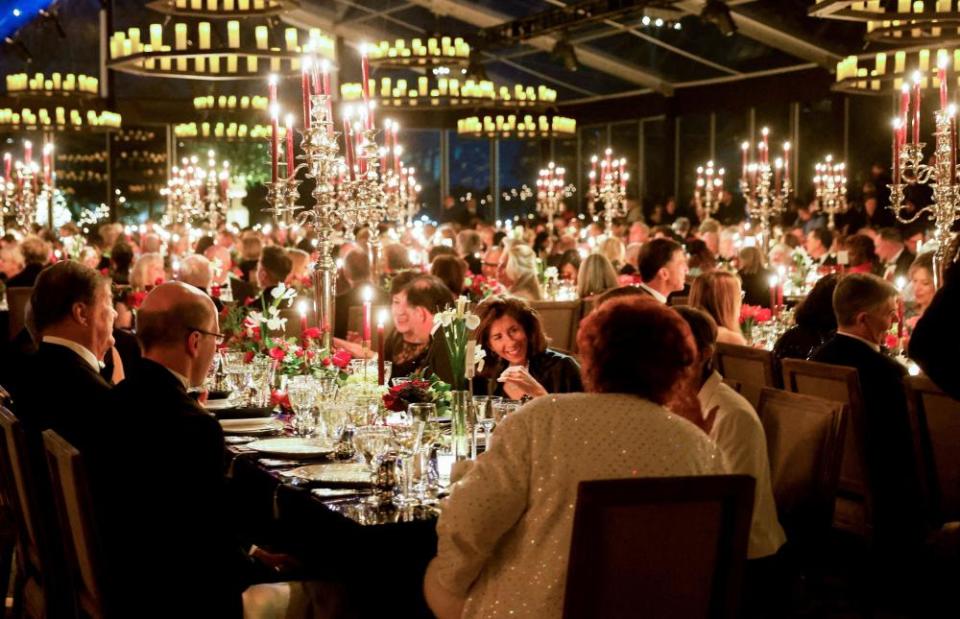 Guests at the White House are seated at tables in a tent on the South Lawn. Several large candelabras rise from each table