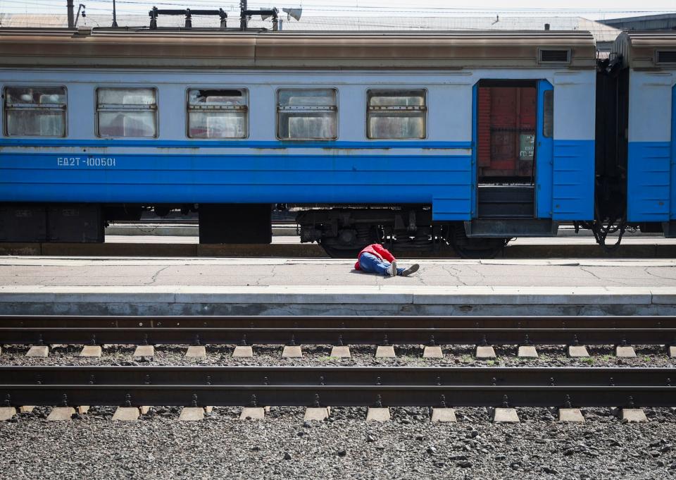 A body on an outdoor train platform in front of blue train cars.