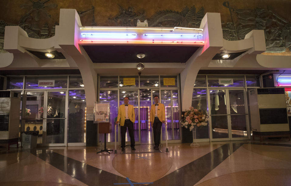 Cinema ushers wear face shields stand outside the entrance to the Scala theater Friday, July 3, 2020 in Bangkok, Thailand. The Scala theater has shut its doors after 51 years as a shrine for Thai movie-goers. (AP Photo/Sakchai Lalit)