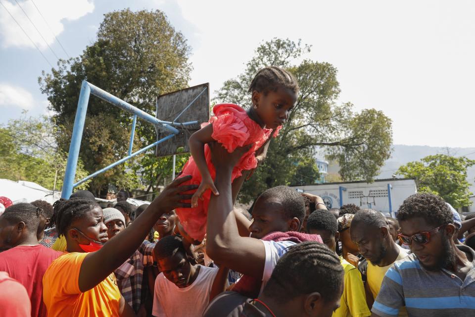 Un padre levanta a su hija hacia la parte delantera de una fila de gente que espera para recibir comida en un albergue para familias desplazadas por la violencia de las pandillas, en Puerto Príncipe, Haití, el 14 de marzo de 2024. (AP Foto/Odelyn Joseph)