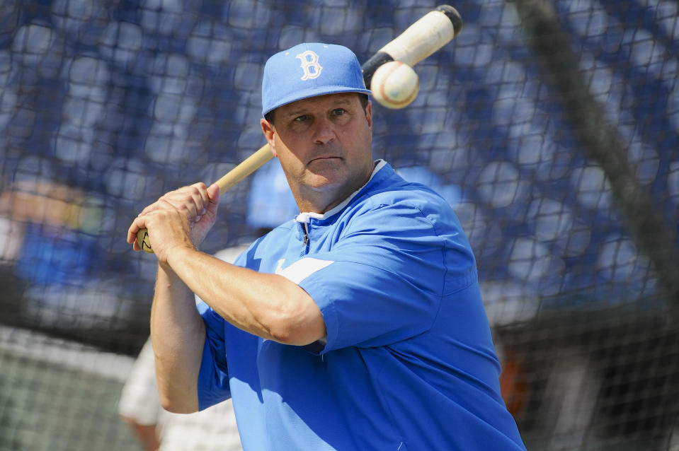 FILE - In this June 14, 2013, file photo, UCLA coach John Savage eyes the ball during NCAA college baseball practice at TD Ameritrade Park in Omaha, Neb. A new rule intended to help speed up the game also could thwart attempts to steal signs in college baseball. The NCAA will allow a pitcher to wear a wristband with a signal card when the season opens Friday, Feb. 14, 2020, allowing him and the catcher to look into the dugout to get pitch calls and eliminating the need for the catcher to relay the call with hand signs. (AP Photo/Eric Francis, File)