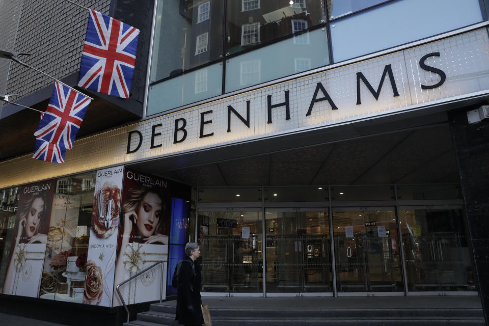 A woman walks past the Debenhams flagship department store on Oxford Street, during England's second coronavirus lockdown in London, Tuesday, Dec. 1, 2020. In another dark day for the British retailing industry, Debenhams said Tuesday it will start liquidating its business after a potential buyer of the company pulled out, a move that looks like it will cost 12,000 workers their jobs. (AP Photo/Matt Dunham)