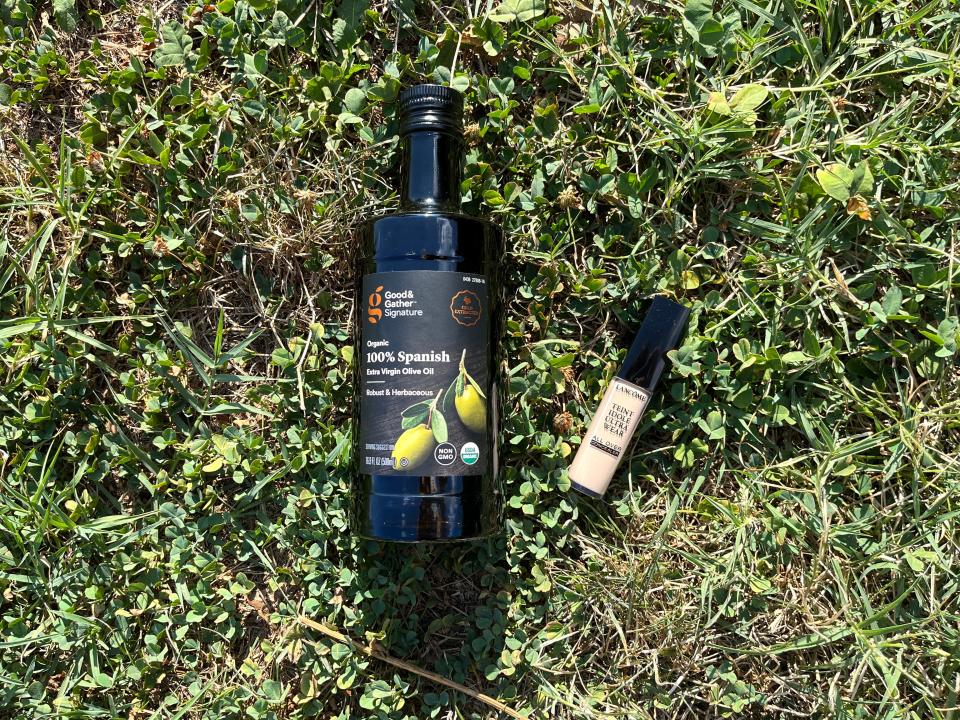 A bottle of olive oil and a tube on concealer laying in the grass