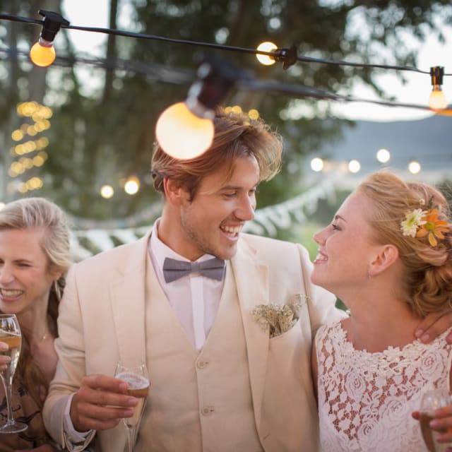 Young couple and their guests with champagne flutes during wedding reception in garden