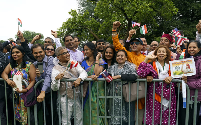 Supporters of Indian Prime Minister Narendra Modi are seen standing behind a fence, holding signs and waving American and Indian flags.