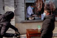 People wearing face masks buy meat from a butcher after the novel coronavirus outbreak in Beijing