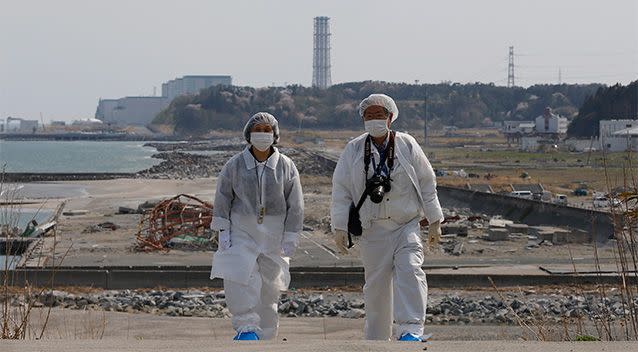Kazuhiro Onuki, right, and his wife, Michiko, wearing white protective gears and filtered masks, walk along the coast damaged by the 2011 tsunami against a backdrop of Fukushima Dai-ni Nuclear Power Plant, that stands south of the crippled Fukushima Dai-ichi nuclear plant. Photo: AP.
