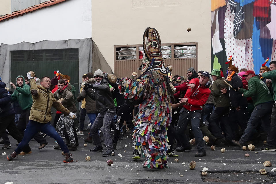 In this photo taken on Sunday, Jan. 19, 2020, people throw turnips at the Jarramplas as he makes his way through the streets beating his drum during the Jarramplas festival in the tiny southwestern Spanish town of Piornal, Spain. The Jarramplas festival features a man in multicolored garb and pointy wooden headgear to shield himself from turnips. A crowd of men in the street pelt the man with the vegetables from close range at the fiesta held annually at Piornal, 200 kilometers west of Madrid, over two days. (AP Photo/Manu Fernandez)