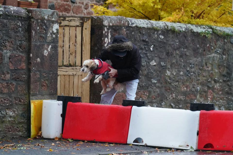 A man lifts his dog over a flood defence barrier erected in Edzell, Scotland (PA)