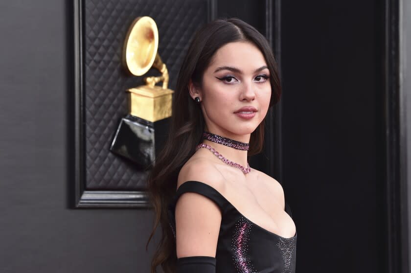 A woman with long, brown hair posing in a black dress and choker