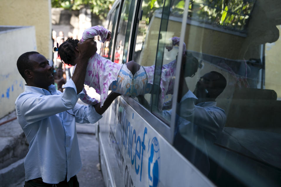 A state worker puts a child into a social services bus after her removal from another branch of the Orphanage of the Church of Bible Understanding, in the Kenscoff area outside Port-au-Prince, Haiti, Friday, Feb. 14, 2020. A fire swept through a nearby orphanage also run by the Pennsylvania-based nonprofit group, killing 15 children, officials said Friday. (AP Photo/Dieu Nalio Chery)