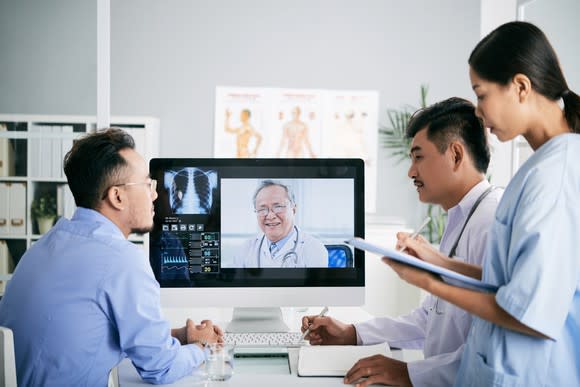 A group of medical interns interacts with a doctor on a monitor.