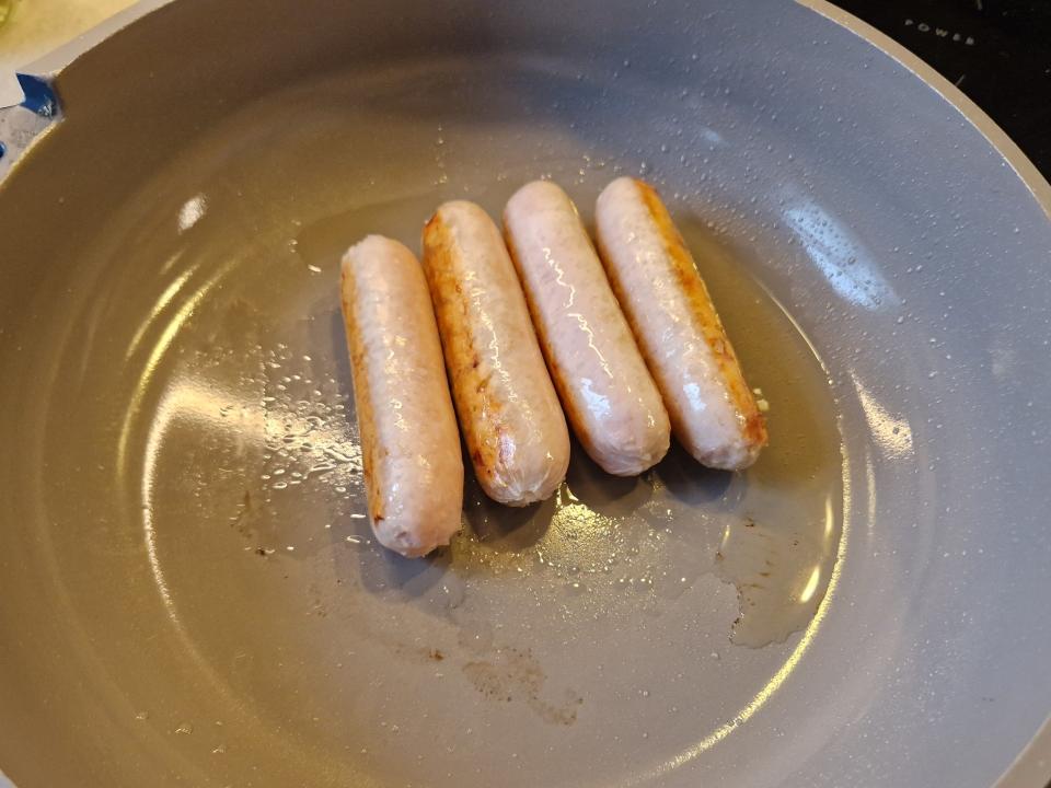four sausage links cooking in a pan on the stove