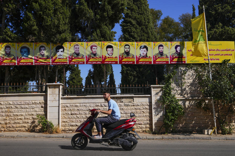 A man rides his scooter as he past by pictures of Hezbollah fighters who were killed in battles with Israel in southern border village of Mays al-Jabal, Lebanon, Tuesday, July 11, 2023. The little village of Ghajar has been a point of contention between Israel and Lebanon for years, split in two by the border between Lebanon and the Israeli-occupied Golan Heights. The dispute has begun to heat up again. (AP Photo/Hassan Ammar)