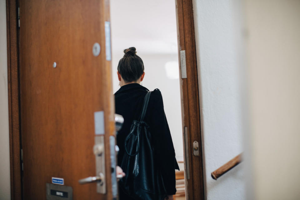 A stock image of a woman entering an apartment through an open door