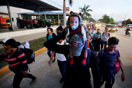 A man carries a child along other Hondurans fleeing poverty and violence, as they move in a caravan toward the United States, in San Pedro Sula, Honduras October 13, 2018. REUTERS/Jorge Cabrera