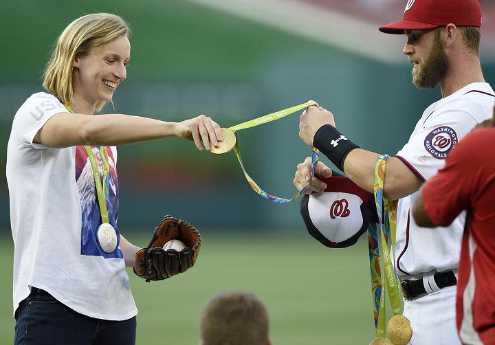 Olympic gold medal swimmer Katie Ledecky hands her medals to Bryce Harper before throwing out the first pitch on Wednesday at Nationals Park. (AP)