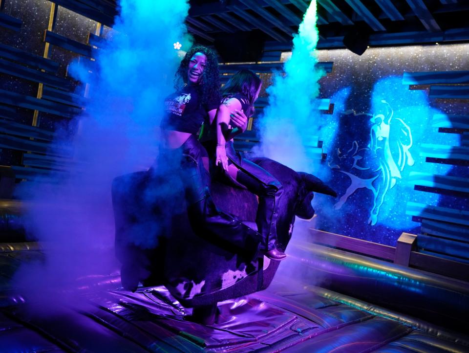 Two employees of PBR Cowboy Bar + Smokehouse ride the mechanical bull during a VIP preview event on Thursday, Feb. 29, 2024, at Easton Town Center.