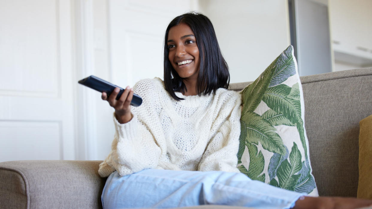  Young Asian woman sat on her sofa watching television 