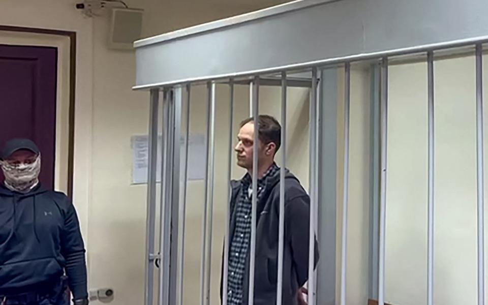 Evan Gershkovich stands inside a defendants' cage during a hearing on the extension of his pre-trial detention