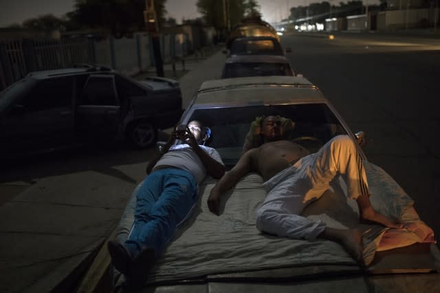 People rest on top of their cars as they wait in line to fill their tanks 