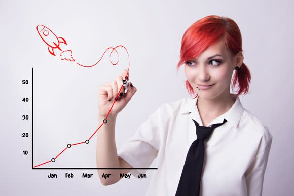 A woman draws a picture of a rocket and an upwardly ascending price chart.