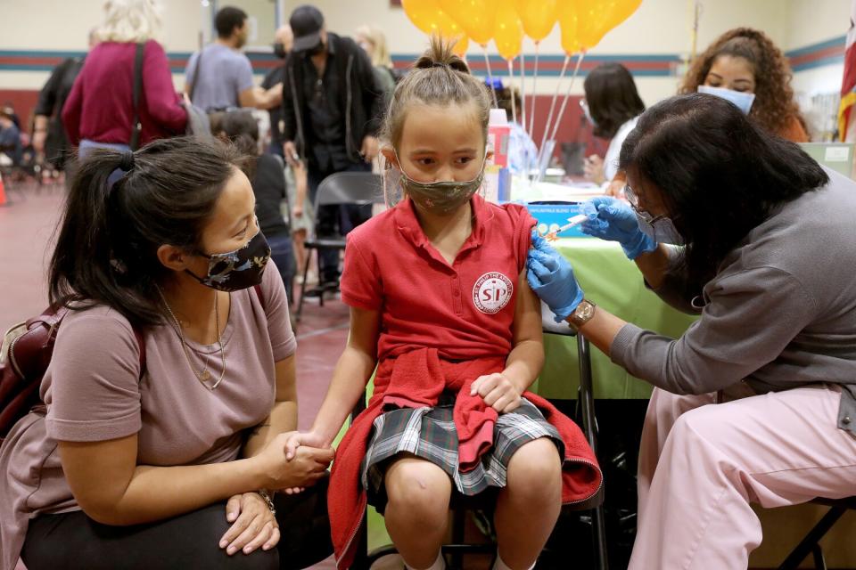 A woman holds the hand of her daughter, who sits in a chair as she receives a shot.