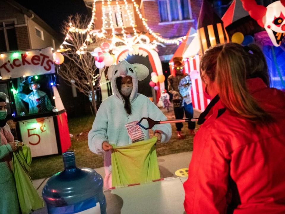 A resident gives out Halloween treats using a reacher-grabber tool as a measure against COVID-19, as part of a fundraiser for the food bank at a decorated home in Ottawa on Halloween night in 2020. (The Canadian Press - image credit)