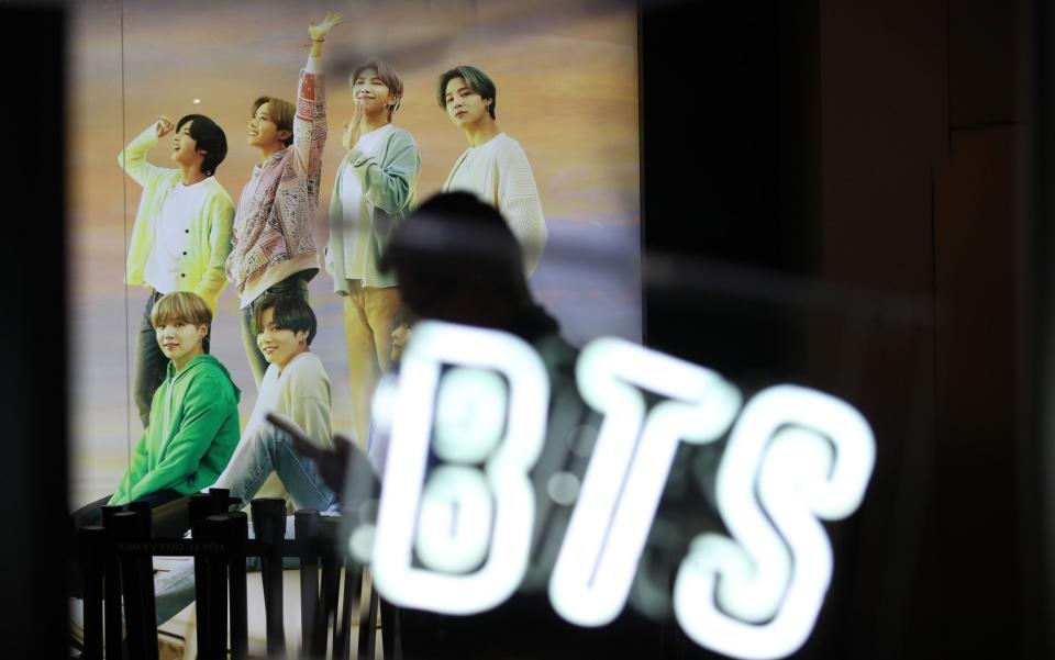 A woman walks past a photo of K-pop boy band BTS at an apartment store in Seoul, South Korea - Shutterstock