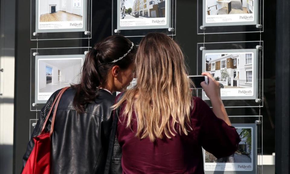 Two young women view properties for sale in an estate agent's window