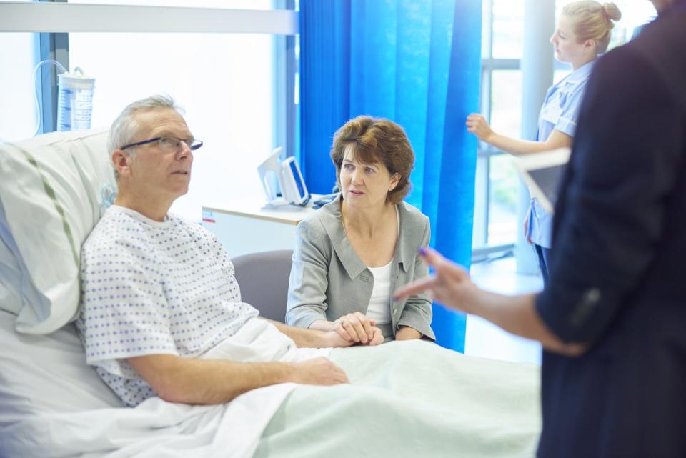 A patient in his hospital bed talks to his spouse and a doctor.