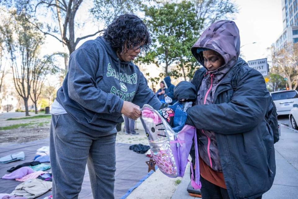 Marsha Robinson de Rancho Cordova ayuda a Monica Win-Cowl con una mochila nueva en la César Chávez Plaza el domingo. Robinson ha estado entregando ropa a las personas sin hogar y necesitados durante los últimos siete años con su esposo.