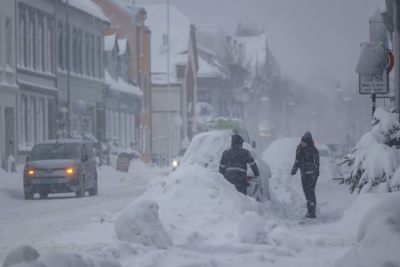 People attempt to clear the snow off a vehicle, in Kristiansand, Norway, Tuesday, Jan. 2, 2024.