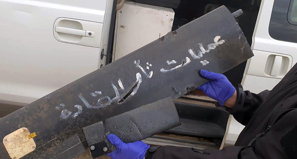 A security official holds part of the wreckage of a drone with Arabic that reads, "revenge operations for our leaders," at Baghdad airport, Iraq, Monday, Jan. 3, 2022. Two armed drones were shot down at the Baghdad airport on Monday, a U.S.-led coalition official said, an attack that coincides with the anniversary of the 2020 U.S. killing of a top Iranian general. (International Coalition via AP)