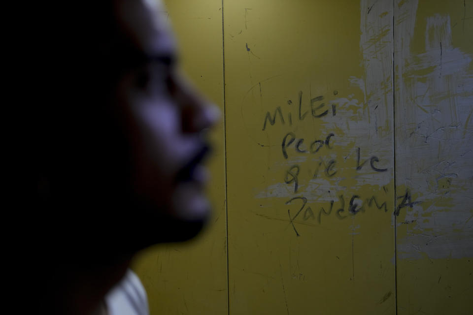 A message on a wall reads in Spanish: "Milei, worse than the pandemic" at the residential building of Ariel Heredia, front, who identifies as non-binary, as he takes the elevator to leave home in Buenos Aires, Argentina, Monday, April 15, 2024. After being fired from the dismantled Women's Ministry as part of President Javier Milei's austerity program, Heredia lost the health insurance needed to access anti-HIV medication. (AP Photo/Natacha Pisarenko)