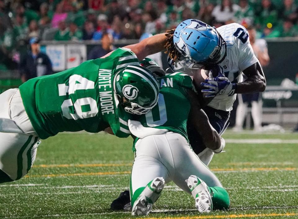 Toronto Argonauts' Deonta McMahon (right) is tackled by Saskatchewan Roughriders' Lake Korte-Moore (49) and Rolan Milligan Jr. (0) during the second half of CFL football action in Regina, on Thursday, July 4, 2024. 