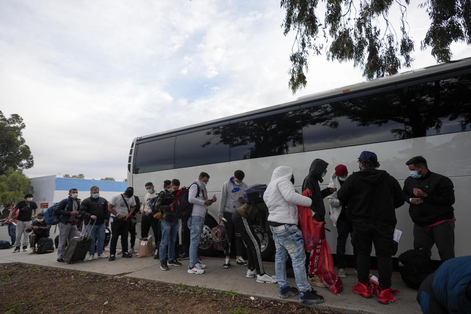 Migrants unload their items off a bus as they arrive at a bus stop after leaving a processing facility, Friday, Feb. 23, 2024, in San Diego. Hundreds of migrants were dropped off Friday at a sidewalk bus stop amid office parks in San Diego with notices to appear in immigration court after local government funding for a reception center ran out of money sooner than expected. (AP Photo/Gregory Bull)