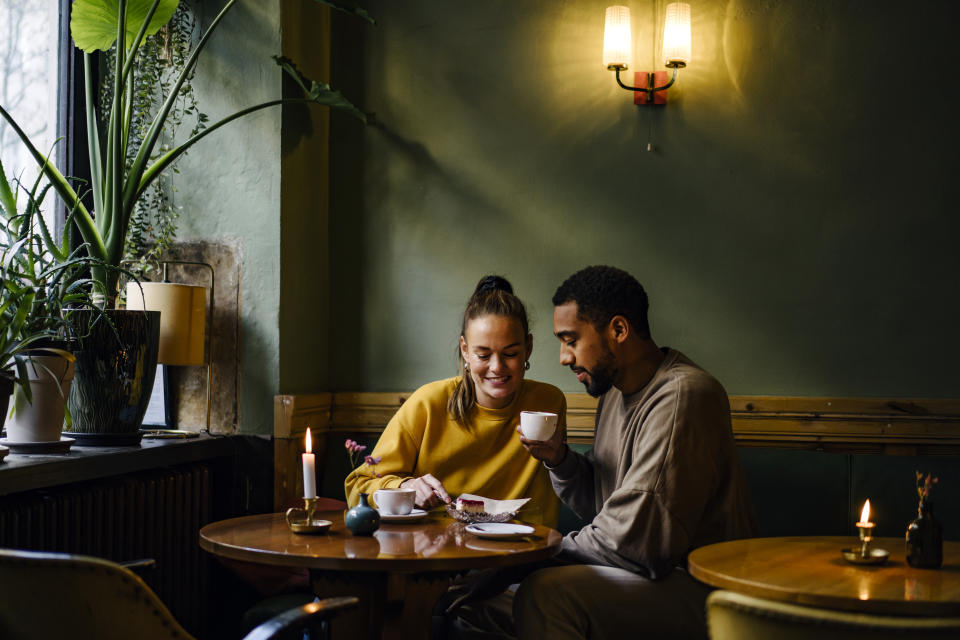 Wide shot with copy space of couple having cappuccinos and cheesecake in coffee shop