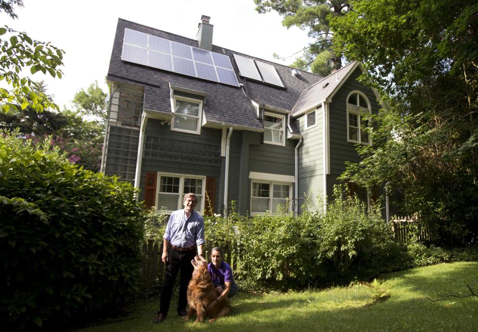 In this Thursday, July 18, 2013 photo, Ketch Ryan, right, and her neighbor Kirk Renaud, pose next her house with solar panels on the roof in Chevy Chase, Md. “In many ways we found that a lot of people were afraid to go solar because they were too afraid of what they didn’t know,” said Ryan, who had a solar energy system installed in her house several years ago. To assist neighbors, Ryan helped establish a cooperative, Common Cents Solar, co-founded with Renaud, “to make sure we didn’t have to reinvent the wheel. We can do it together and we can do it more efficiently,” she said. (AP Photo/Manuel Balce Ceneta)