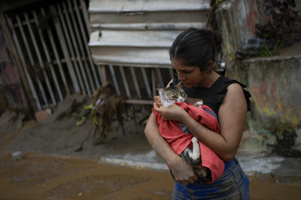 Karen Salinas holds her cat next to her home damaged by flooding in Las Tejerias, Venezuela, Sunday, Oct. 9, 2022. (AP Photo/Matias Delacroix)
