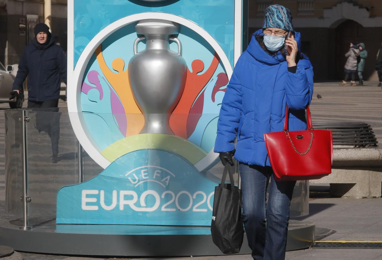 A woman wears a medical mask walks past a sign with Euro 2020 emblem in St.Petersburg where UEFA planned to host four UEFA EURO 2020 matches, including a quarter final, in Russia, Tuesday, March 17, 2020. UEFA today announced the postponement of its flagship national team competition, UEFA EURO 2020, due to be played in June and July this year, avoiding placing any unnecessary pressure on national public services involved in staging matches. For some people the new COVID-19 coronavirus causes only mild or moderate symptoms, but for some it can cause more severe illness. (AP Photo/Dmitri Lovetsky)