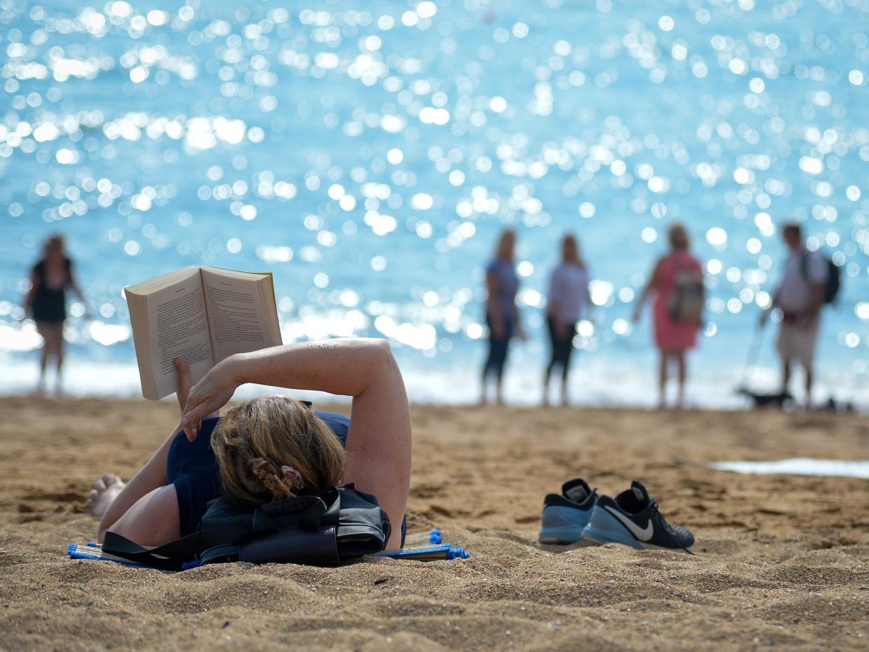 Woman reads book with arm shielding face on UK beach with ocean in background