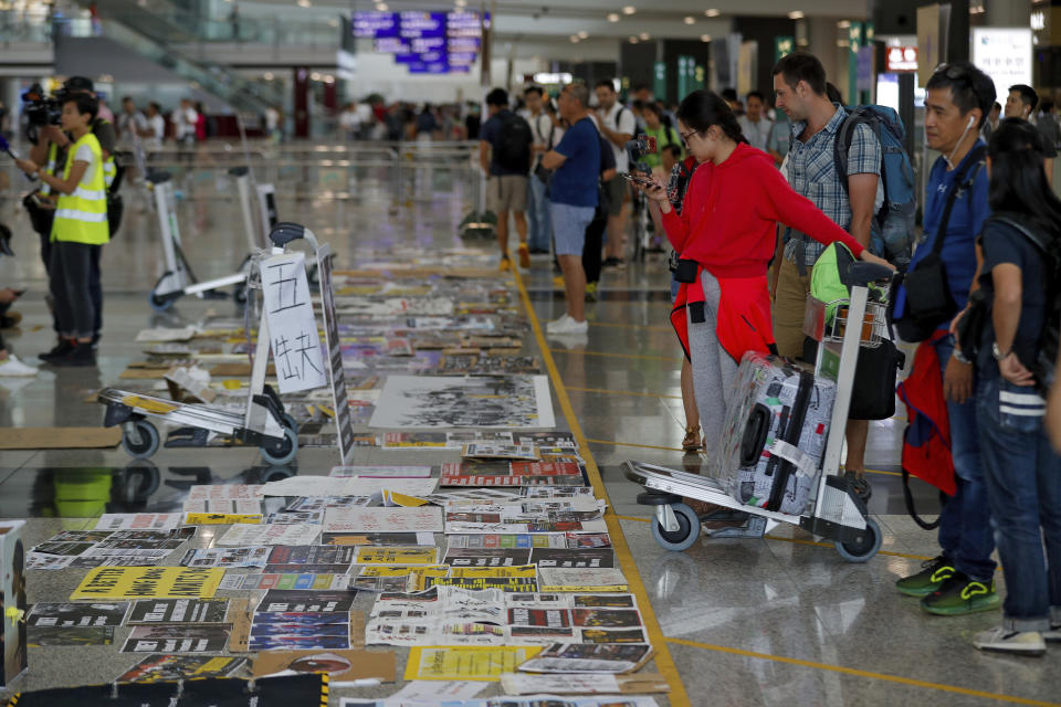 Travellers look at placards and posters placed by protesters at the airport in Hong Kong, Wednesday, Aug. 14, 2019. Flight operations resumed at the airport Wednesday morning after two days of disruptions marked by outbursts of violence highlighting the hardening positions of pro-democracy protesters and the authorities in the Chinese city that's a major international travel hub. (AP Photo/Vincent Thian)