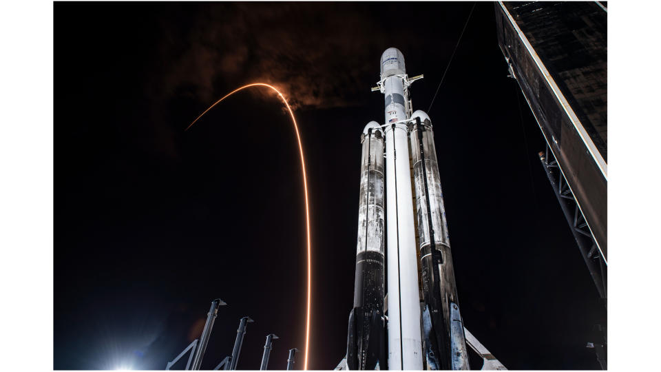 a falcon 9 rocket carves an orange arc in the sky behind a black-and-white falcon heavy rocket