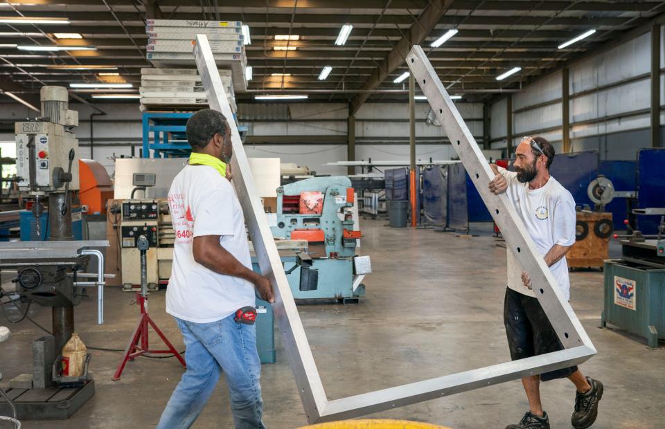 Desmond Davis, left, and Christopher Legini carry framing for flood gates they are building at Savannah Flood Control in Riviera Beach, Florida on May 5, 2022.