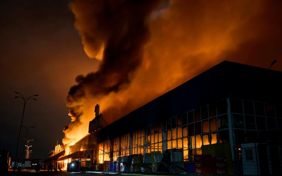 Plumes of smoke rise above the shelled out shopping centre, which is lit by orange flames - AP Photo/LIBKOS