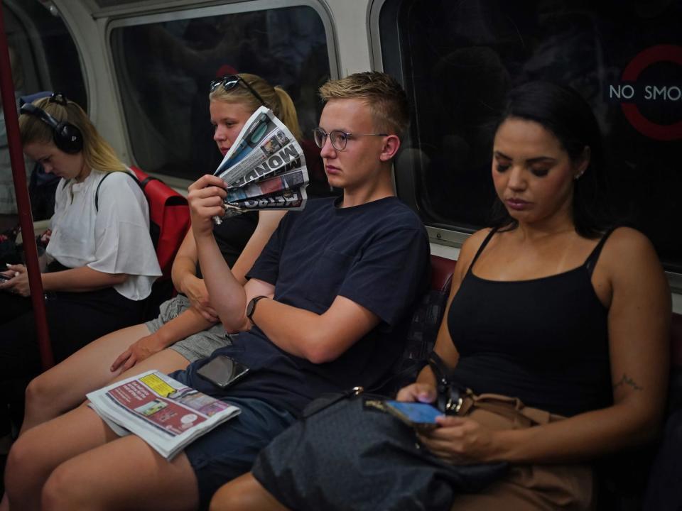 A man uses a newspaper to cool himself while on the tube.