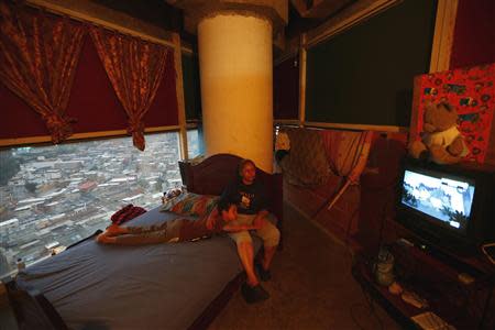 Adriana Gutierrez and her son Carlos Adrian watch TV as they sit on their bed in their 24th floor apartment inside the "Tower of David" skyscraper in Caracas February 3, 2014. REUTERS/Jorge Silva